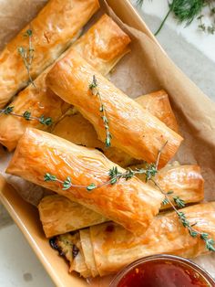 some food is sitting in a box with sauce on the side and green sprigs