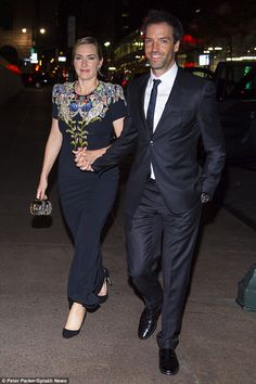 a man and woman are walking down the street at night, dressed in formal attire