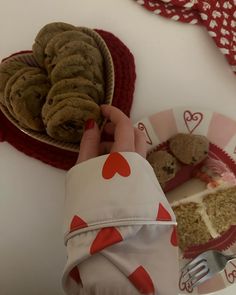 a person holding up a cookie in front of a heart shaped plate with cookies on it