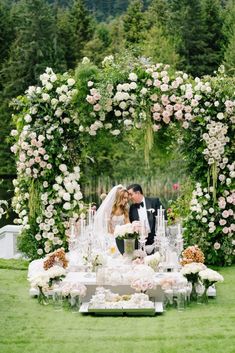 a bride and groom are kissing in front of an outdoor wedding ceremony arch with flowers