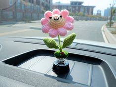 a crocheted pink flower sitting on top of a car dash board next to a window