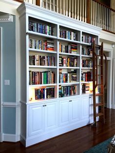 a ladder is in front of a bookcase with many books on it and two windows