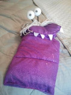 a purple bag with googly eyes and teeth on it sitting on top of a bed