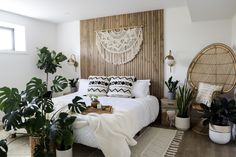 a bedroom with white bedding, plants and wicker baskets on the floor in front of it