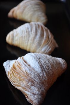 three croissants with powdered sugar on them sitting on a black surface