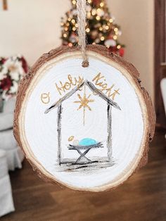 a christmas ornament with a nativity scene hanging from a tree branch in front of a christmas tree