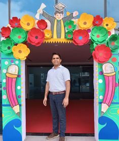 a man standing in front of a colorful archway decorated with paper flowers and a graduate's cap