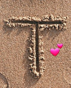 the letter t is written in the sand with two hearts