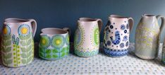 five vases are lined up on a tablecloth with blue and green flowers painted on them