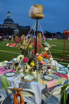 a table set up with plates and flowers on it at a football game in the evening