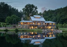 a large house sitting on top of a lush green hillside next to a lake at night