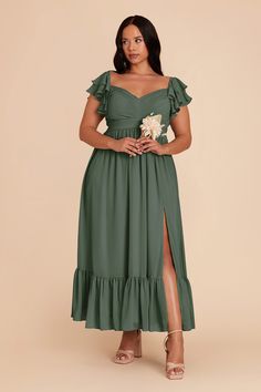 a woman wearing a green dress with ruffles on the side and a flower in her hand