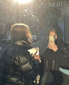 two people standing in the rain taking pictures with their cell phones