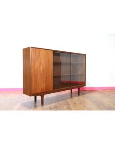 a wooden cabinet sitting on top of a hard wood floor next to a pink wall