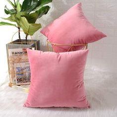 two pink pillows sitting on top of a bed next to a plant