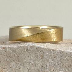 a yellow gold wedding ring sitting on top of a stone block in front of a white wall