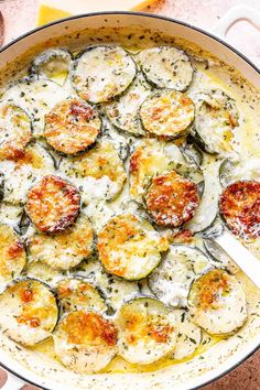 a pan filled with cooked zucchini and cheese on top of a table next to some bread