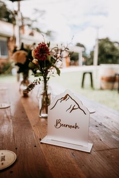 a wooden table topped with a vase filled with flowers and a sign that says berrosh