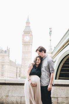 a pregnant couple standing next to each other in front of the big ben clock tower