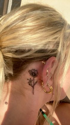 a woman with a flower tattoo on her left side behind her ear is looking down at the ground