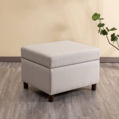 a white ottoman sitting on top of a hard wood floor next to a potted plant