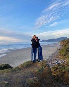 two people standing on the beach hugging each other