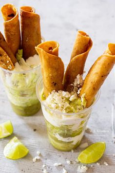 two small cups filled with food and garnished with limes on the side