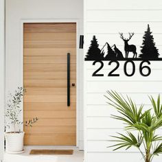 a wooden door with a deer and trees on it, next to a potted plant