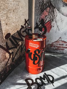 an orange barrel with graffiti on it sitting in front of a wall