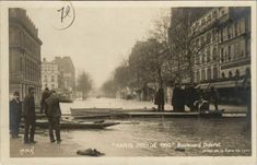 an old black and white photo of people standing on the side of a river with boats in it