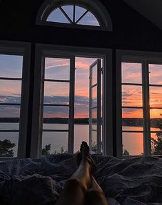 a person laying in bed with their feet up against the window looking out at water