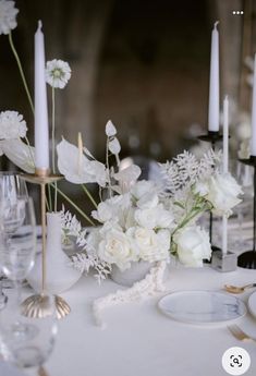 the table is set with white flowers, candles and other items for an elegant dinner