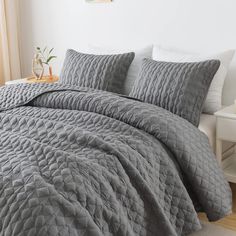 a bed with grey comforter and pillows in a room next to a white wall