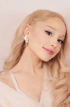 a woman with long blonde hair wearing large gold earrings and a white fur coat is posing for the camera