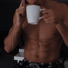 a shirtless man drinking from a white cup