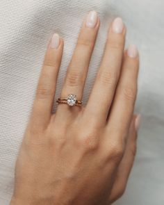 a woman's hand with a diamond ring on her left hand, resting against a white cloth