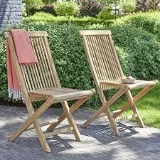 two wooden chairs sitting next to each other on a brick floor in front of bushes