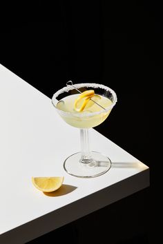 a martini with lemon wedges on a white countertop next to a slice of lemon