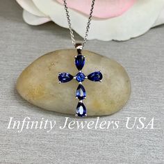 "The pendant pictured is a lab created blue sapphire cross #6073 Also shown with lab created ruby #6867 -Approximate total carat weight: approx. 1.40ctw diamond equivalent -Center Stone Size: 3mm - approx. 0.10ct diamond equivalent -Center Stone Shape: round -Accent Stone Size: 5x3mm approx. 0.26ct each diamond equivalent -Accent Stone Shape: 5 pear shape stones -Gem Type: lab created sapphire -Stone Clarity: VS2 -Stone Color: Blue -Moh's Scale: 9 hardness -Metal Type and Purity: 14k white gold Blue Cross Jewelry For Anniversary, Pear-shaped Sapphire Necklaces For Anniversary, Pear-shaped Sapphire Necklace For Wedding, Blue Pear-shaped Diamond Necklace, Blue Sterling Silver Cross Necklace Gift, Blue Cross Pendant Necklace For Anniversary, Pear-shaped Sapphire Gemstone Necklace, Blue Pear-shaped Sapphire Necklace, Blue Gemstone Cross-shaped Jewelry