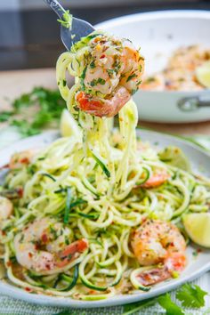 a fork full of shrimp and zucchini pasta being lifted from a white plate