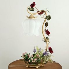 a vase with flowers on top of a table next to a light fixture that is hanging from the ceiling