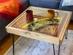 This stunning 25x25" Mandala Coffee Table uses a series of 9 different, individually stained and painted layers to create a beautiful and complex design, utilizing reds, oranges, yellows and greens to create a warm color palette that will be at home in any living room or office. The table is framed using rustic stained pine. The piece is capped with a sturdy 1/4" tempered glass panel, with rounded edges for safety. Piece will be shipped with legs removed, but pre-drilled holes on the table base Hippie Coffee Tables, Eclectic Coffee Table Wood, Stained Glass Coffee Table, Spanish Tile Coffee Table, Trippy Coffee Table, Reclaimed Wood Decor, Puzzle Table, Hippie Decor, Warm Colour Palette