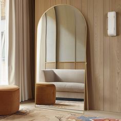 a mirror sitting on top of a wooden floor next to a chair and ottoman in front of a window