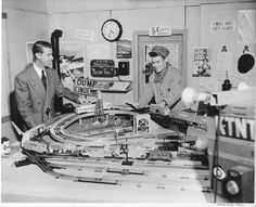 black and white photograph of two men working on a model train set