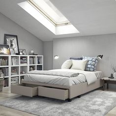 a bed sitting under a skylight in a bedroom next to a book shelf filled with books