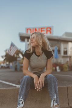 a woman sitting on the side of a cement wall in front of a diner sign