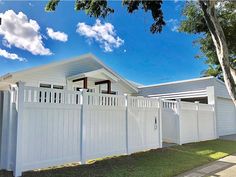 a white fence is in front of a house with trees and grass on the side