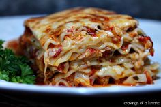 a white plate topped with lasagna covered in sauce and cheese next to parsley