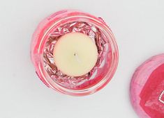 a pink jar with a candle inside on a white surface next to a red heart