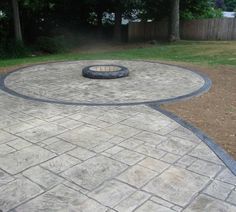 an outdoor fire pit in the middle of a brick patio with grass and bushes behind it